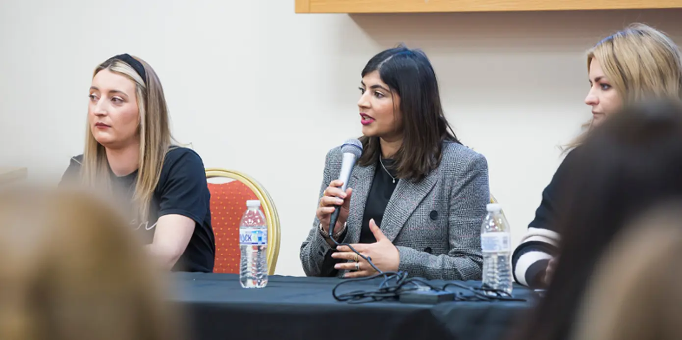 Three women sat at a table with one holding a microphone